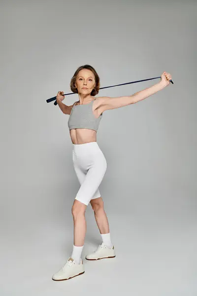 Uma mulher madura em top branco e shorts golpeia uma pose com um bastão de esqui. — Fotografia de Stock