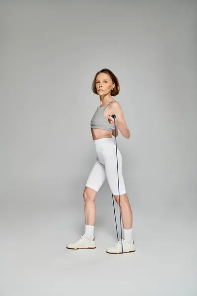 Mature woman in active wear holding skipping rope against white background. — Stock Photo