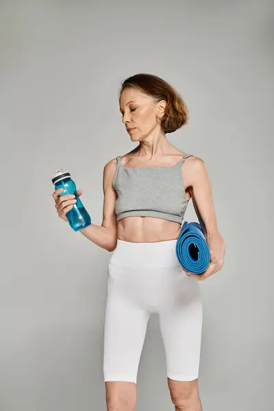 Active woman elegantly holding yoga mat and water bottle. — Stock Photo