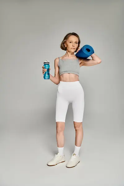 Strong woman in comfortable clothing holding a yoga mat and water bottle. — Stock Photo