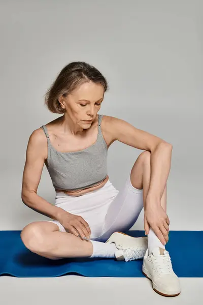 Une femme mature en tenue confortable s'assoit paisiblement sur un tapis de yoga, faisant de l'exercice et posant activement. — Photo de stock