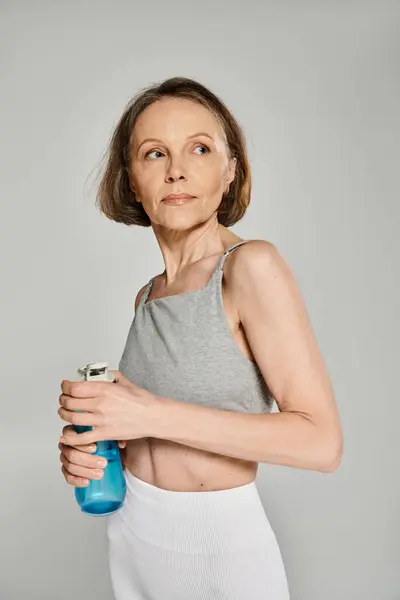 Femme active en tenue confortable tenant une bouteille d'eau sur fond gris. — Photo de stock