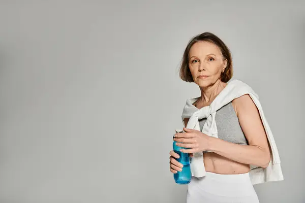 Femme plus âgée dans des vêtements confortables sirote sereinement d'une bouteille d'eau. — Photo de stock
