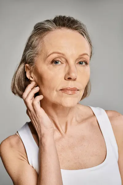 Mujer con estilo en tanque blanco golpeando una pose reflexiva con la mano en la barbilla. - foto de stock