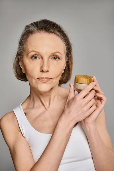 A mature attractive woman in comfy attire holds a jar of cream gracefully. — Stock Photo