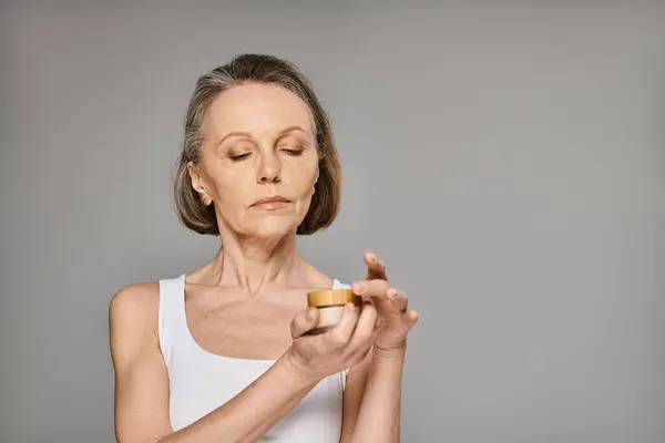 A mature woman in comfy attire gracefully holds a container of cream. — Stock Photo