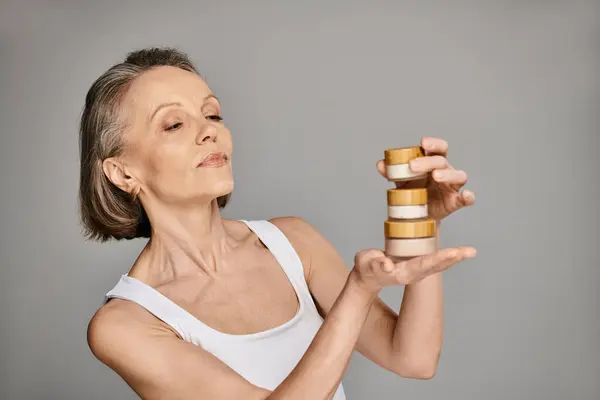 A mature woman in comfortable clothing gracefully holds a bottle of cream. — Stock Photo