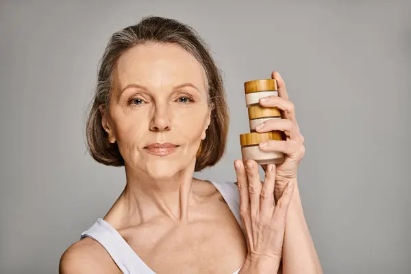 Mujer madura sosteniendo dos frascos de productos para el cuidado de la piel. - foto de stock