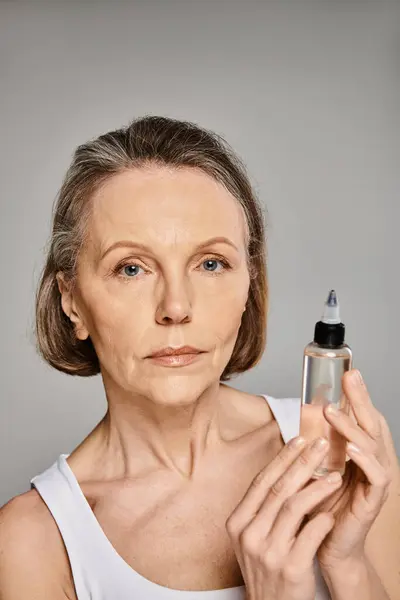 Une femme mature et séduisante en tenue confortable tient gracieusement une bouteille de produit de soin de la peau. — Photo de stock