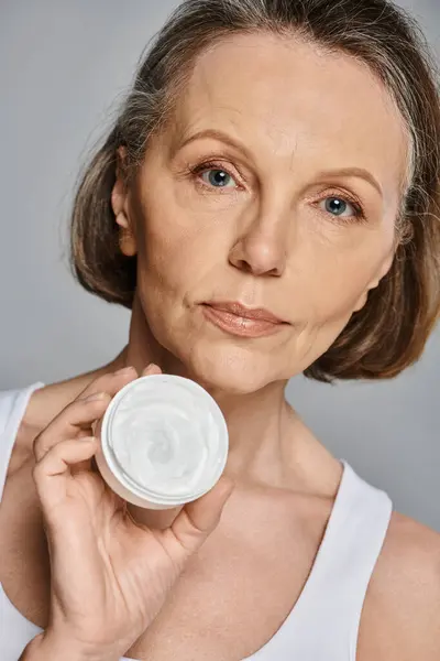 A stylish mature woman holding a container of cream in hand. — Stock Photo