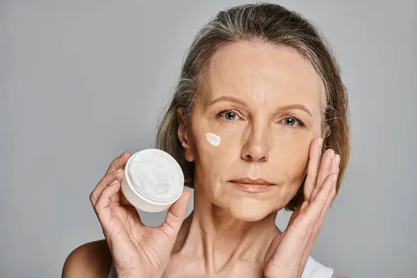 Woman in comfy attire gently applies cream to her face. — Stock Photo
