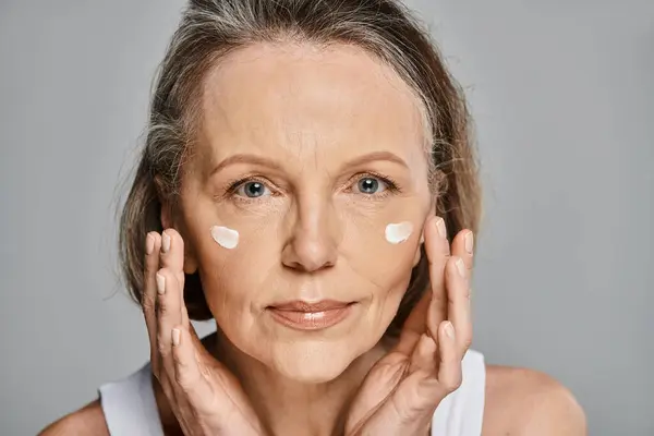 An older woman serenely applying cream to her face. — Stock Photo