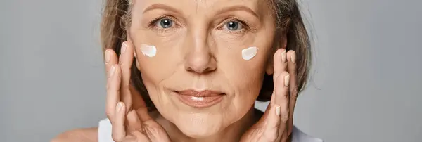 Eine elegante Frau cremt ihr Gesicht sanft für eine verjüngende Hautpflege ein. — Stockfoto