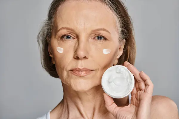 A woman enhancing her skin by gracefully applying cream. — Stock Photo