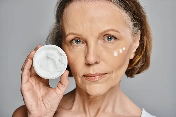 An elegant woman gently applies cream to her face, enhancing her natural beauty. — Stock Photo
