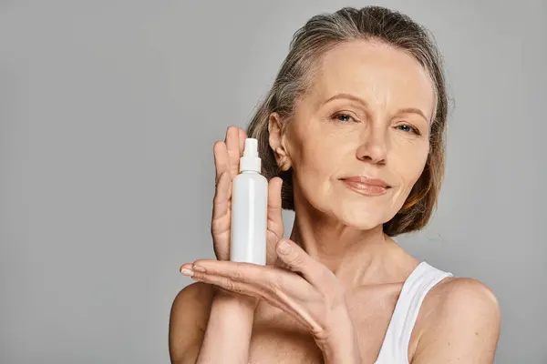A mature woman in comfy attire holding a spray bottle in her hand, actively posing. — Stock Photo