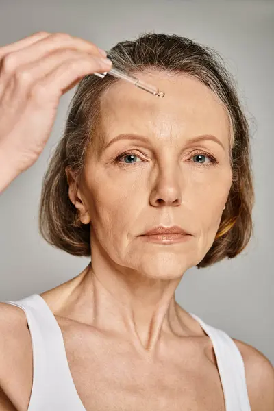 Une femme applique soigneusement un sérum sur son visage, en se concentrant sur sa routine de soins de la peau. — Photo de stock