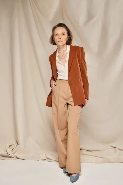 Стильная зрелая женщина в коричневом пиджаке и брюках, позирует уверенно и изящно. — стоковое фото