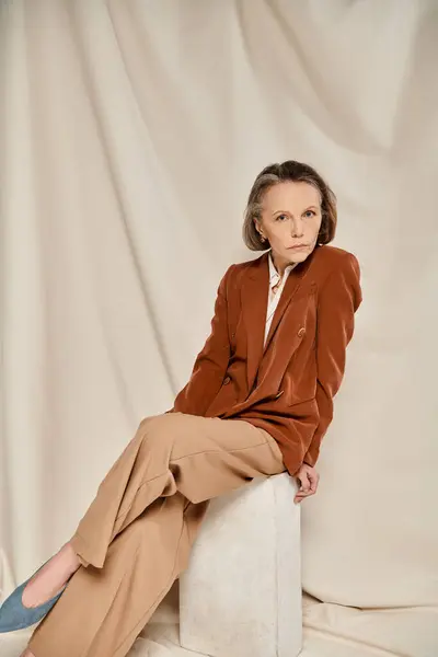 Mature woman in tan blazer sits gracefully on a cube in thought. — Stock Photo