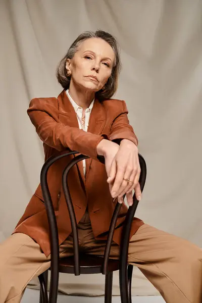 Mature, attractive woman lounging on chair in brown blazer and tan pants. — Stock Photo