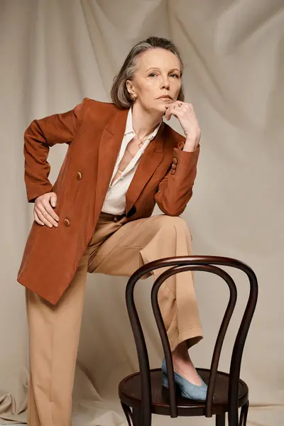 Mature woman poses actively in tan blazer and pants on chair. — Stock Photo