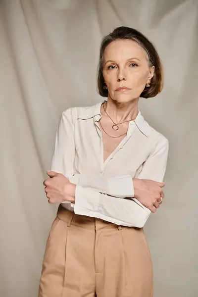 A mature woman in white shirt and tan trousers poses gracefully. — Stock Photo