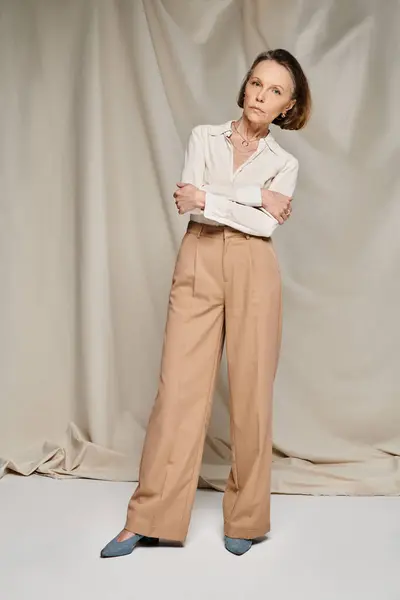 A mature woman in a stylish white blouse and tan trousers poses gracefully. — Stock Photo
