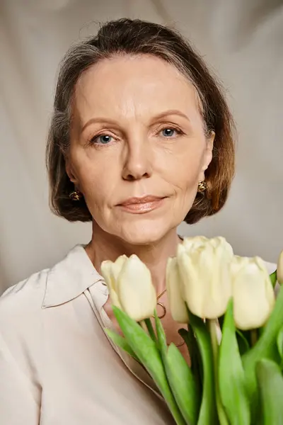 A mature woman gracefully holds a bouquet of white tulips. — Stock Photo