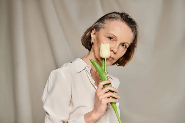 Mature woman in comfy attire holds tulip gracefully. — Stock Photo