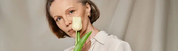 A mature woman in casual attire holding a flower in her mouth while posing energetically. — Stock Photo