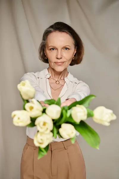 A mature woman gracefully holds a bouquet of white tulips, exuding elegance and grace. — Stock Photo