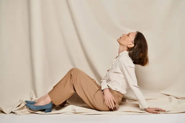 Una donna in camicia bianca e pantaloni abbronzanti siede con grazia su un letto. — Foto stock