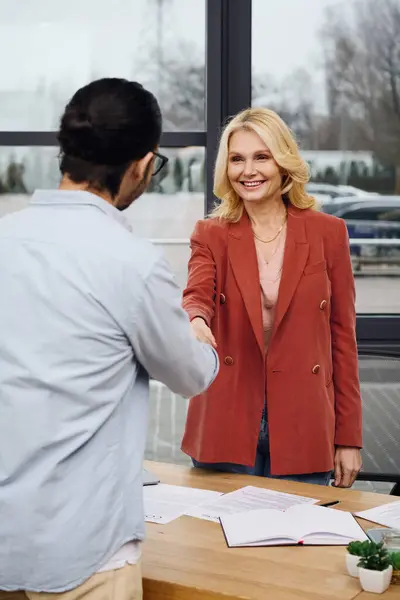 Una mujer y un hombre se dan la mano en una oficina durante una entrevista de trabajo. - foto de stock