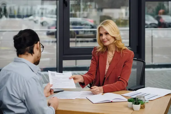 Eine Frau reicht einem Mann am Schreibtisch Papiere. — Stockfoto