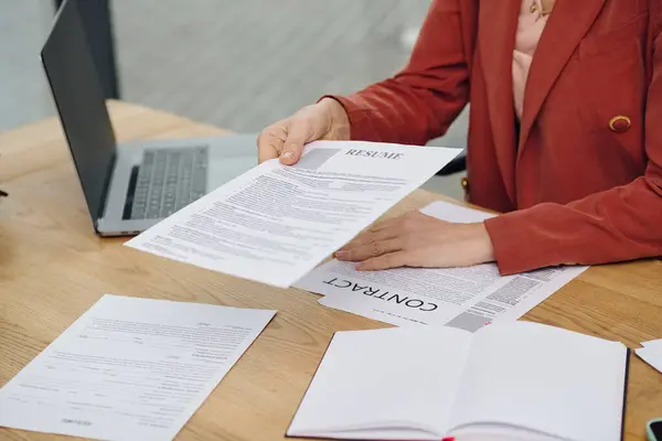 Mujer examina cuidadosamente un curriculum vitae sentado en un escritorio. - foto de stock