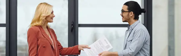 A man and woman exchanging documents in front of a window. — Stock Photo