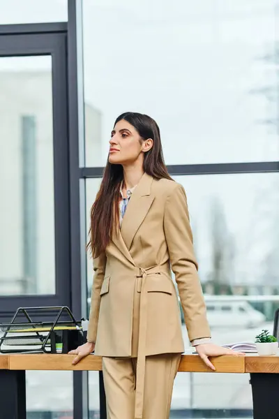 Eine Frau im braunen Anzug steht selbstbewusst vor einem Schreibtisch. — Stockfoto