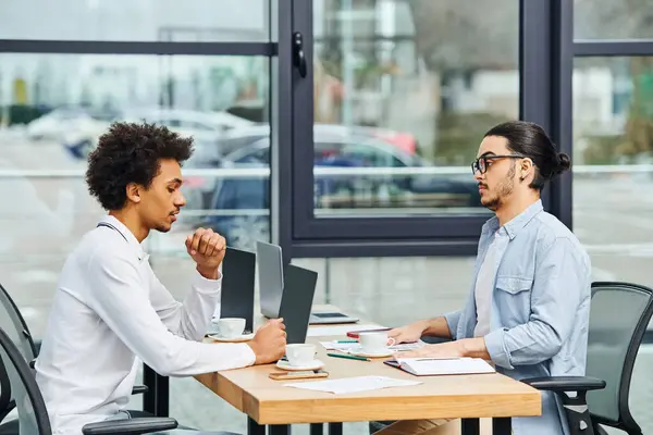 Dos hombres conversando animadamente en una mesa de oficina. - foto de stock