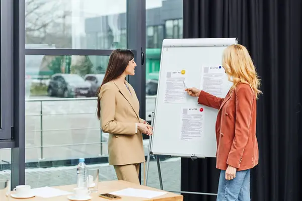 Two business women discussing ideas in front of a whiteboard. — Stock Photo