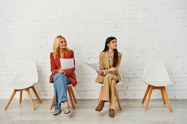Un grupo de mujeres sentadas con gracia en sillas frente a una pared de ladrillo. - foto de stock