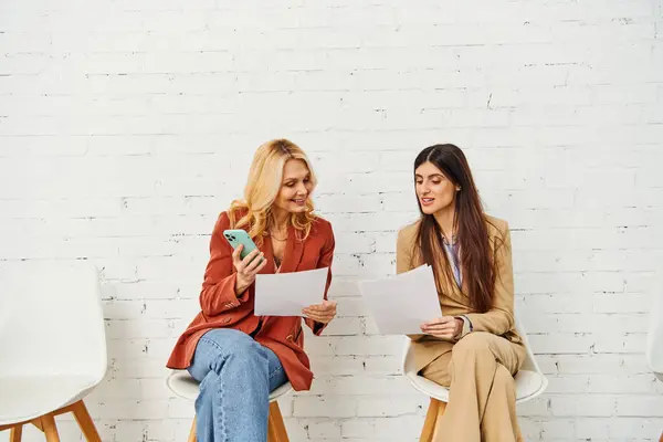 Dos mujeres sentadas, absortas en papeles. - foto de stock