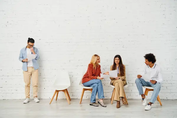 A group of attractive people sitting on chairs in front of a white wall. — Stock Photo