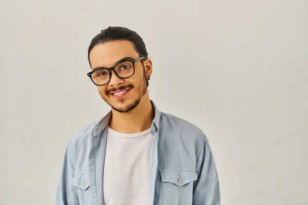 A young man with glasses and blue shirt poses confidently. — Stock Photo