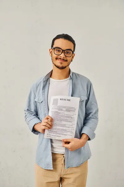 Un homme debout devant un mur blanc, tenant son CV. — Photo de stock