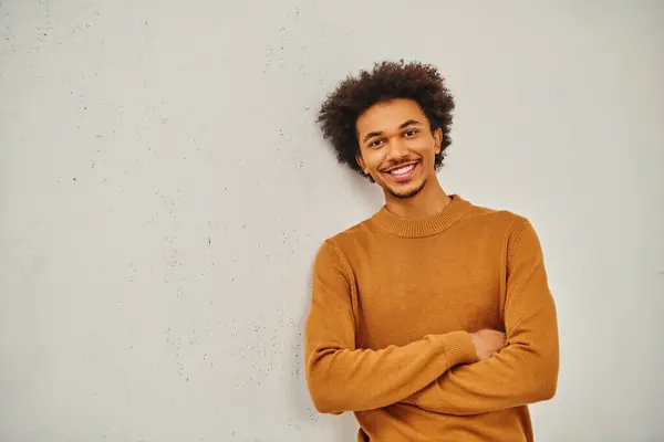 Un jeune homme élégant dans un pull bronzé appuyé avec désinvolture contre un mur. — Photo de stock