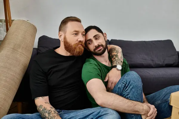 A couple of men sit comfortably on top of a couch in their new home — Stock Photo