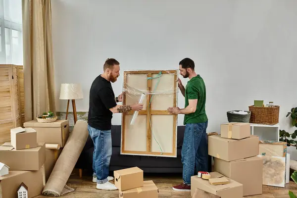 Zwei Männer packen in einem gemütlichen Wohnzimmer voller Kisten liebevoll Möbel aus und beginnen gemeinsam ihr neues Leben. — Stockfoto