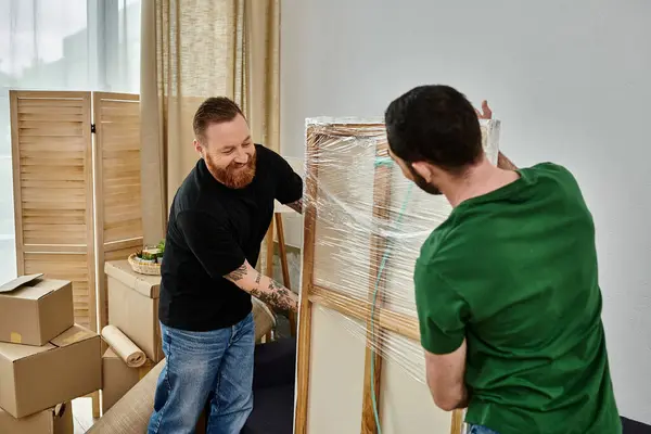 Ein schwules verliebtes Paar steht in der Nähe eines Rahmens in seinem neuen Zuhause, umgeben von Umzugskartons. — Stockfoto