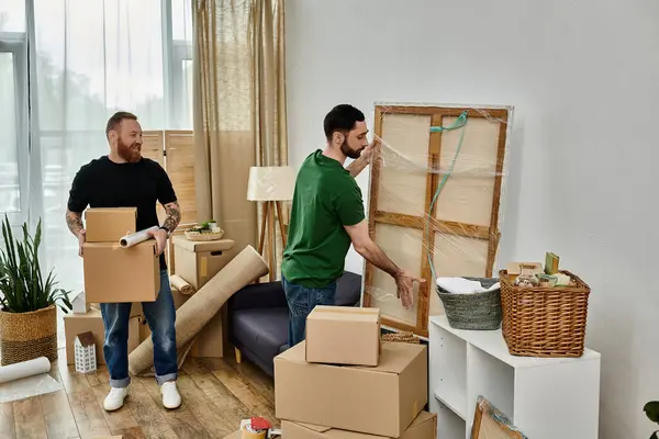 Zwei Männer, ein schwules Paar, arrangieren Umzugskartons in einem Wohnzimmer, während sie ein neues Kapitel in ihrem Leben beginnen. — Stockfoto
