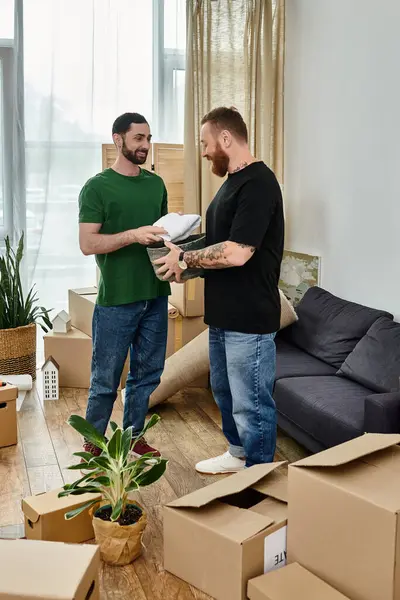Una coppia gay innamorata si trova nel loro nuovo soggiorno, circondata da scatole, abbracciando l'emozione di un nuovo inizio. — Foto stock